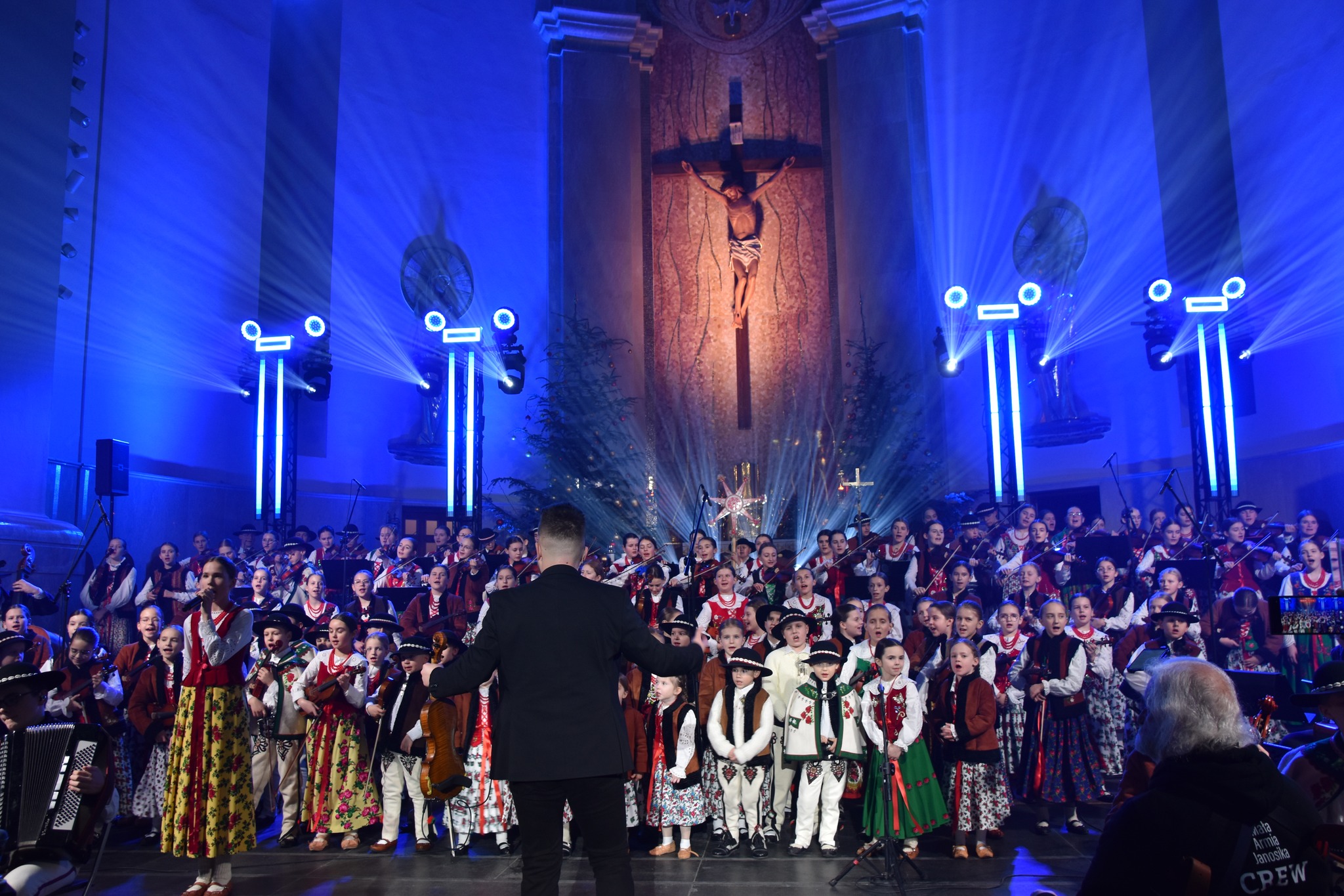 Dzieci z Małej Armii Janosika stoją na scenie a przed nimi dyrygent